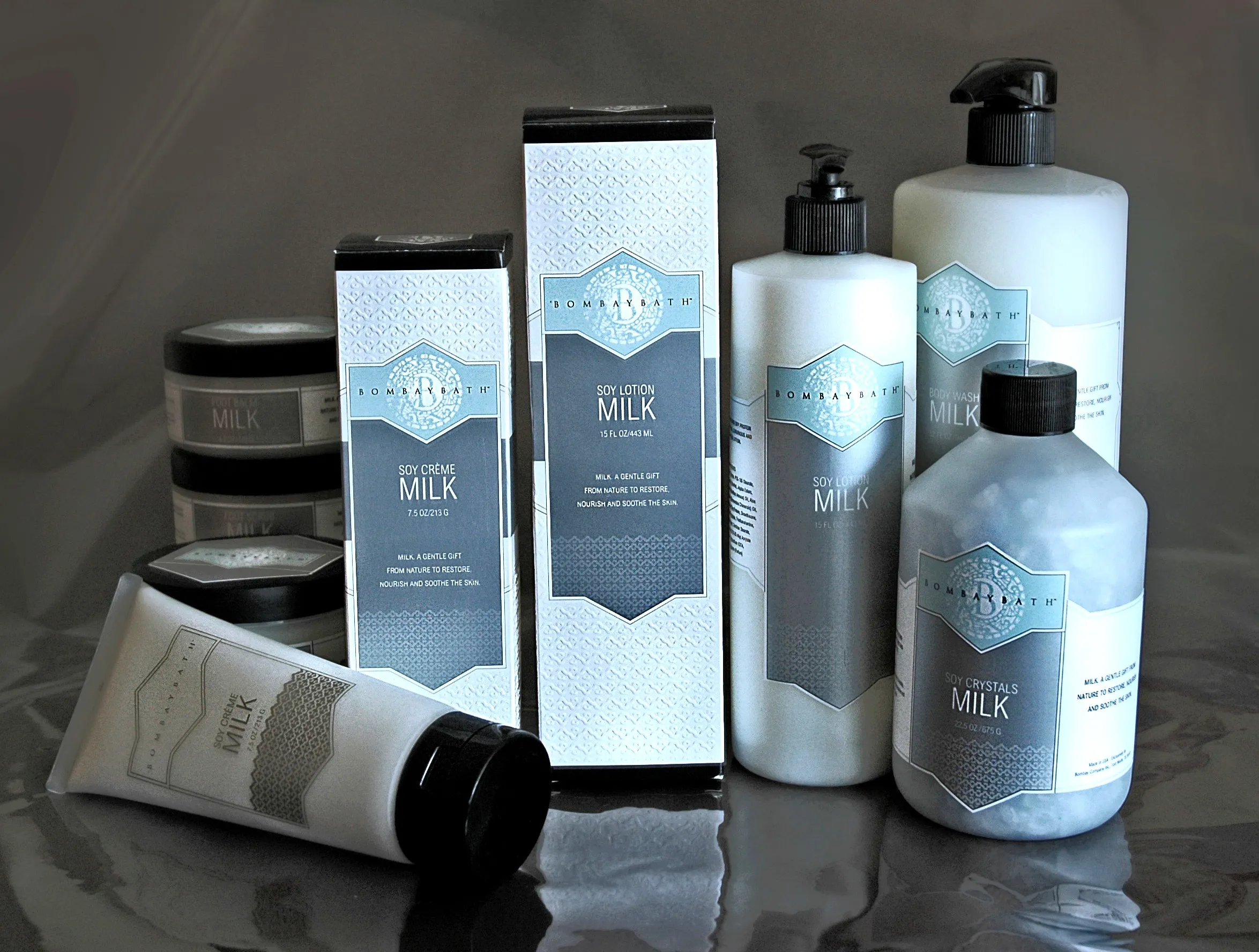 The full Bombay Bath Milk lineup on a reflective surface: soy crème and soy lotion cartons, pump bottles, jars, and a tube, all in pale blue and white.