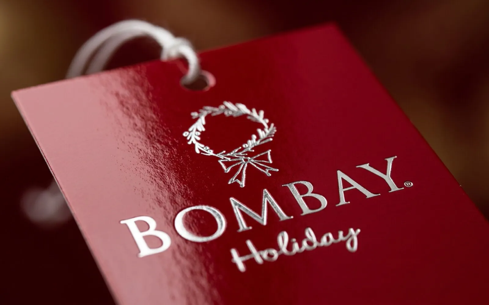Bombay Holiday glossy red price tag with a silver-foil wreath logo and wordmark.