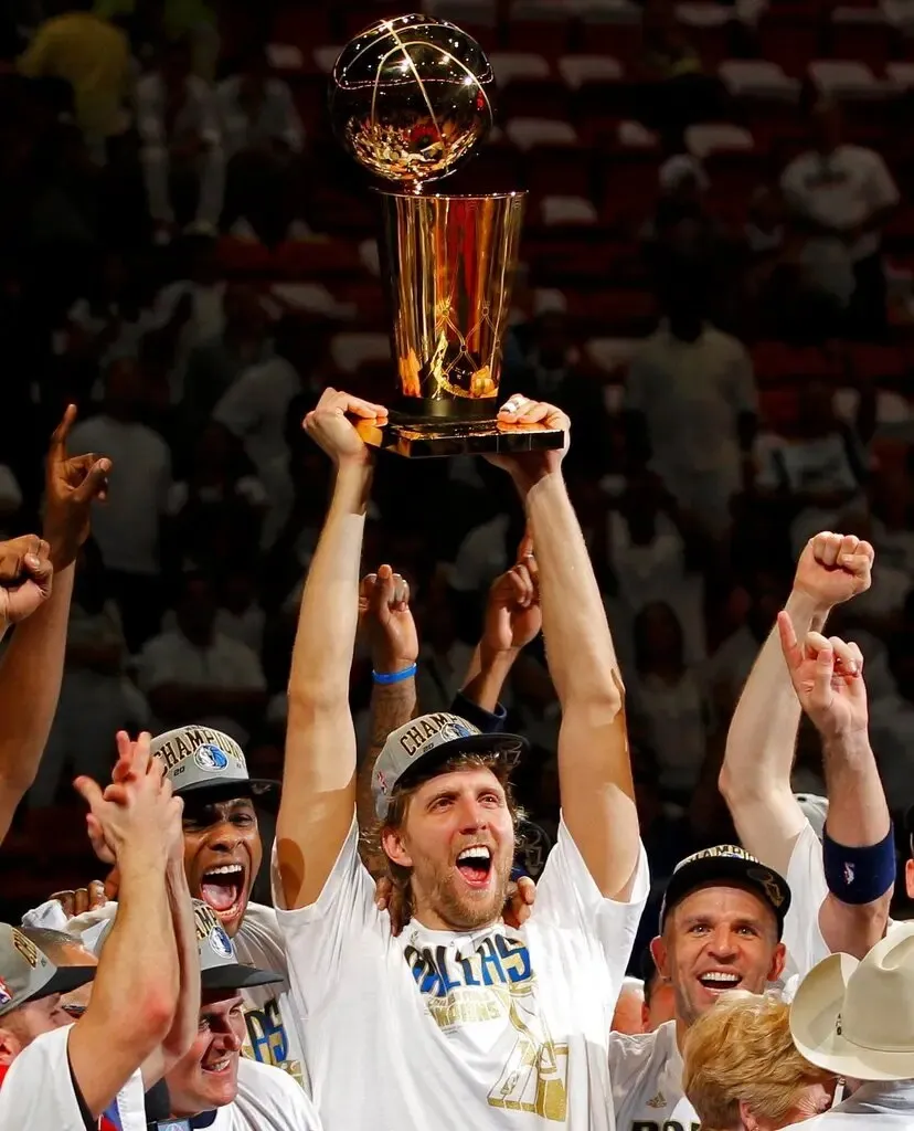Dirk Nowitzki lifts the 2011 NBA Finals trophy as teammates celebrate.