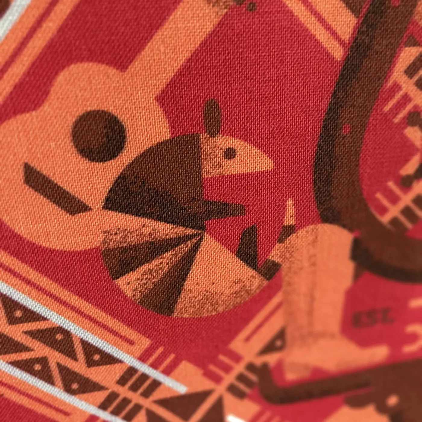 Macro detail of the printed cloth, a guitar and armadillo motif filling the frame, the weave visible through the ink.